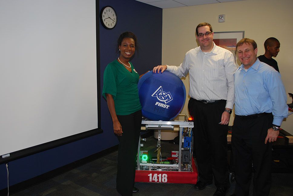 Three adults posing with the 1418 robot and a catapult ball.